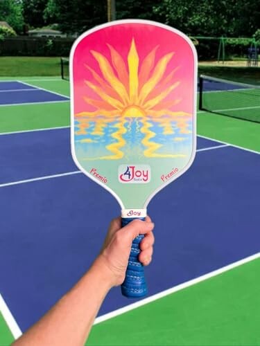 Hand holding a colorful pickleball paddle on a tennis court.