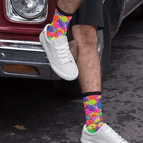 Person wearing colorful socks and white sneakers near a red vehicle.