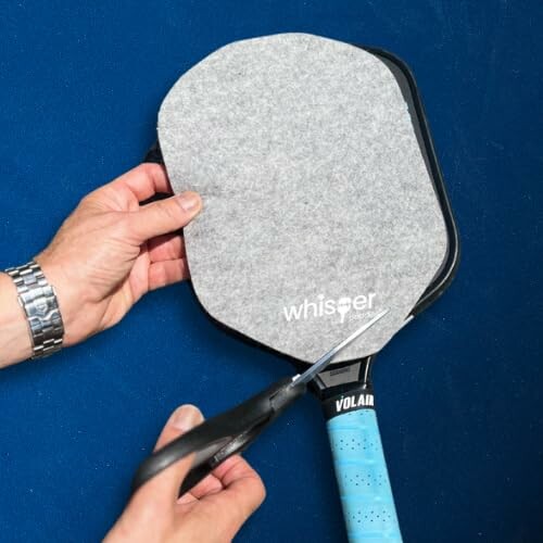 Hands cutting gray cover on pickleball paddle with scissors.