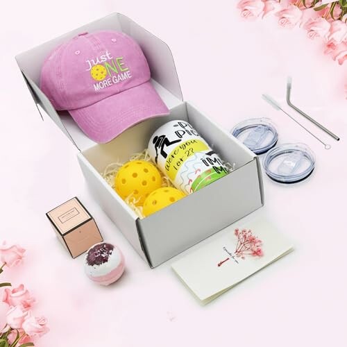 Gift box containing a pink hat, yellow balls, tumbler, and various accessories.