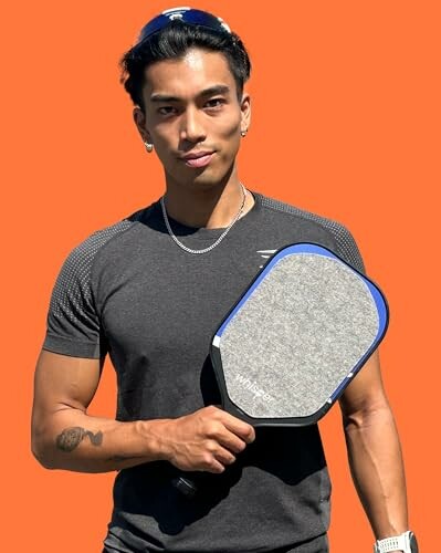 Man holding a pickleball paddle against an orange background