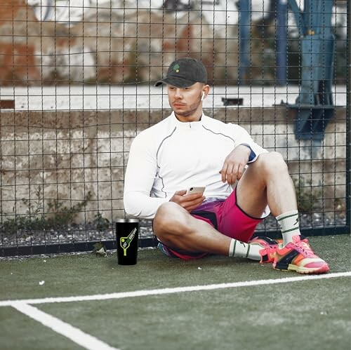 Man sitting on sports field with phone and sports drink