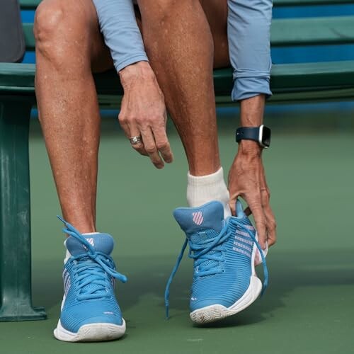 Person tying blue sneakers on a bench.