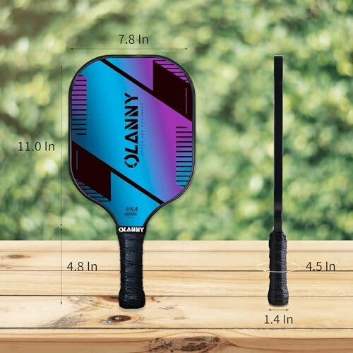 Colorful pickleball paddle with measurements against a blurred outdoor background.