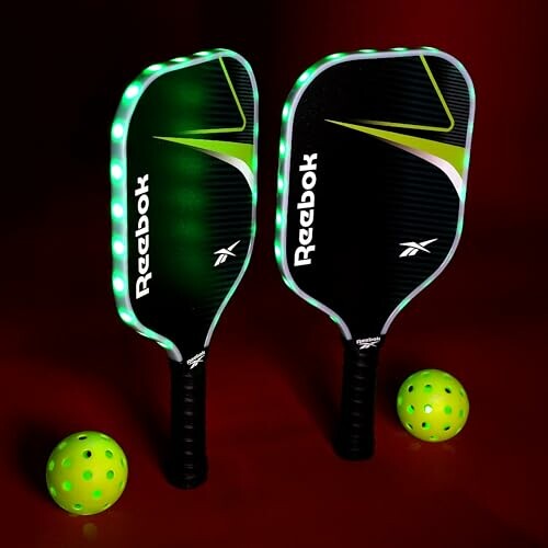 Two Reebok pickleball paddles with green lights and two green pickleballs on a red background.