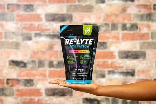 Hand holding a Re-Lyte Hydration variety pack against a brick wall.