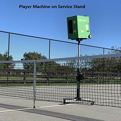 Tennis ball machine on court with net and fence.