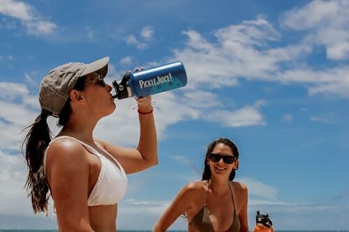 Two women on a beach, one drinking from a bottle.